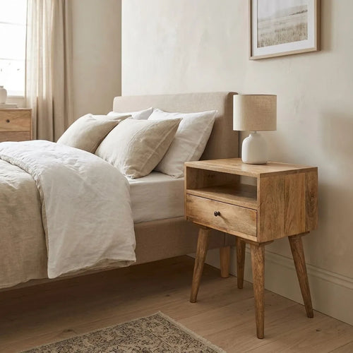 Bedside Table beside a bed with linen bedding, with a table lamp on top