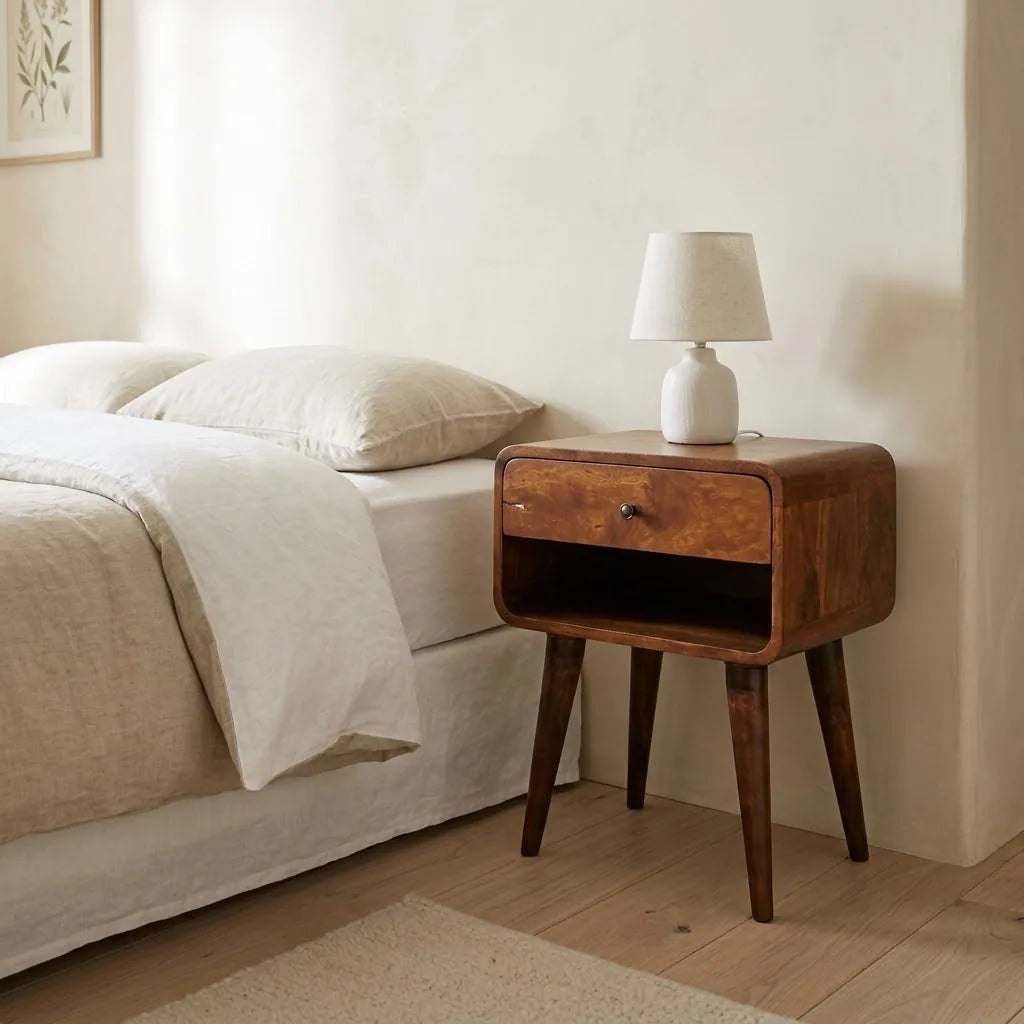Curved Bedside Table beside a bed with linen bedding, with a table lamp on top