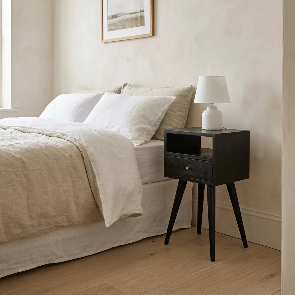 Small Black Bedside Table beside a bed with linen bedding, with a table lamp on top