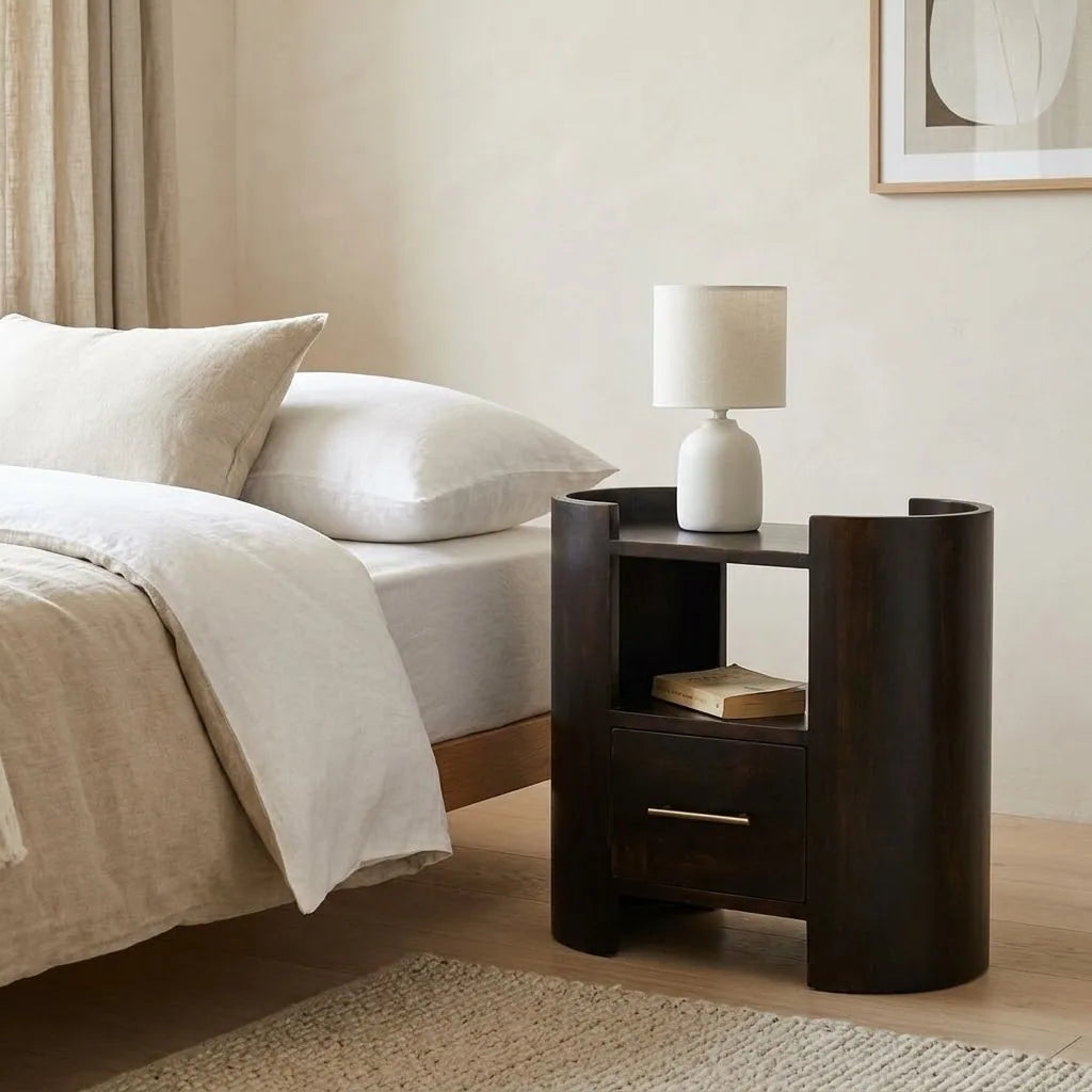 Wide Dark Bedside Table beside a bed with linen bedding, with a table lamp on top